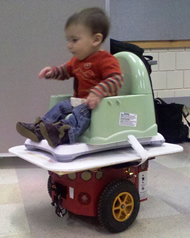 Image shows the set up for our balance board control method.  The infant sits in the commercial seat on top of the balance board, supported by the custom platform.